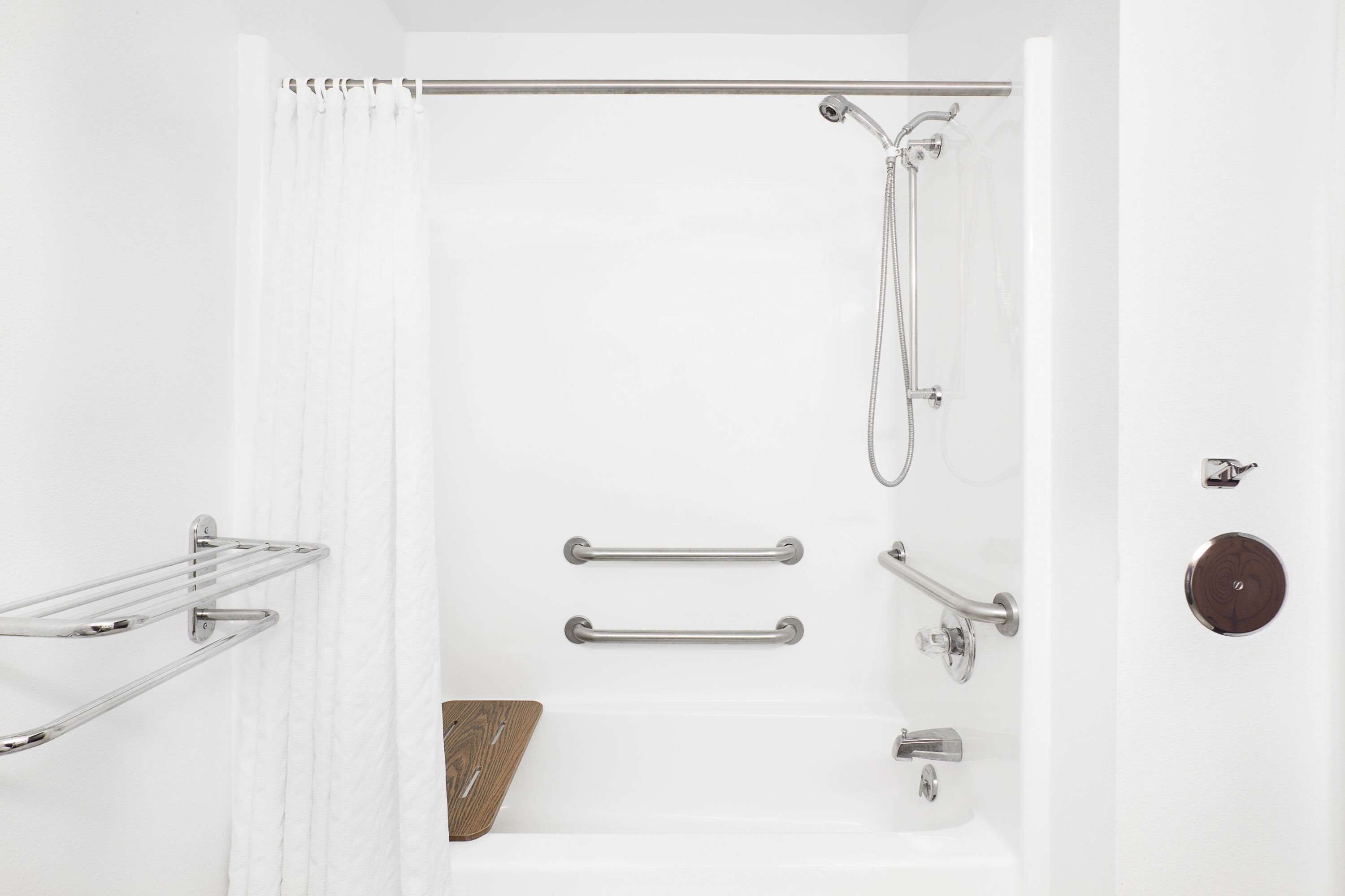 Un baño moderno con ducha, barras de apoyo, un perchero para toallas y un tapete de baño de madera.
