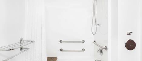 Un baño moderno con ducha, barras de apoyo, un perchero para toallas y un tapete de baño de madera.