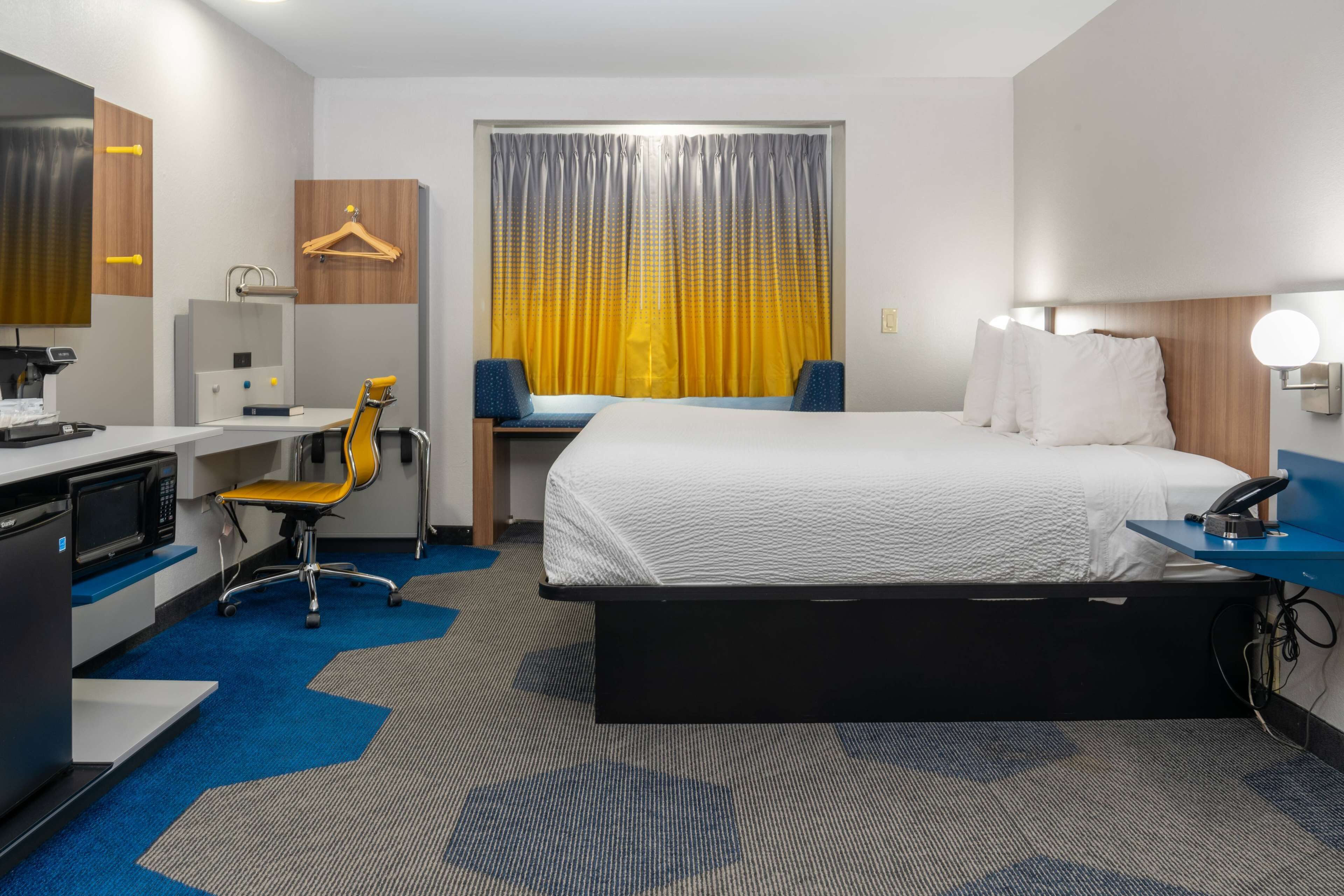 A hotel room with a bed, desk, chair, and a small kitchenette.