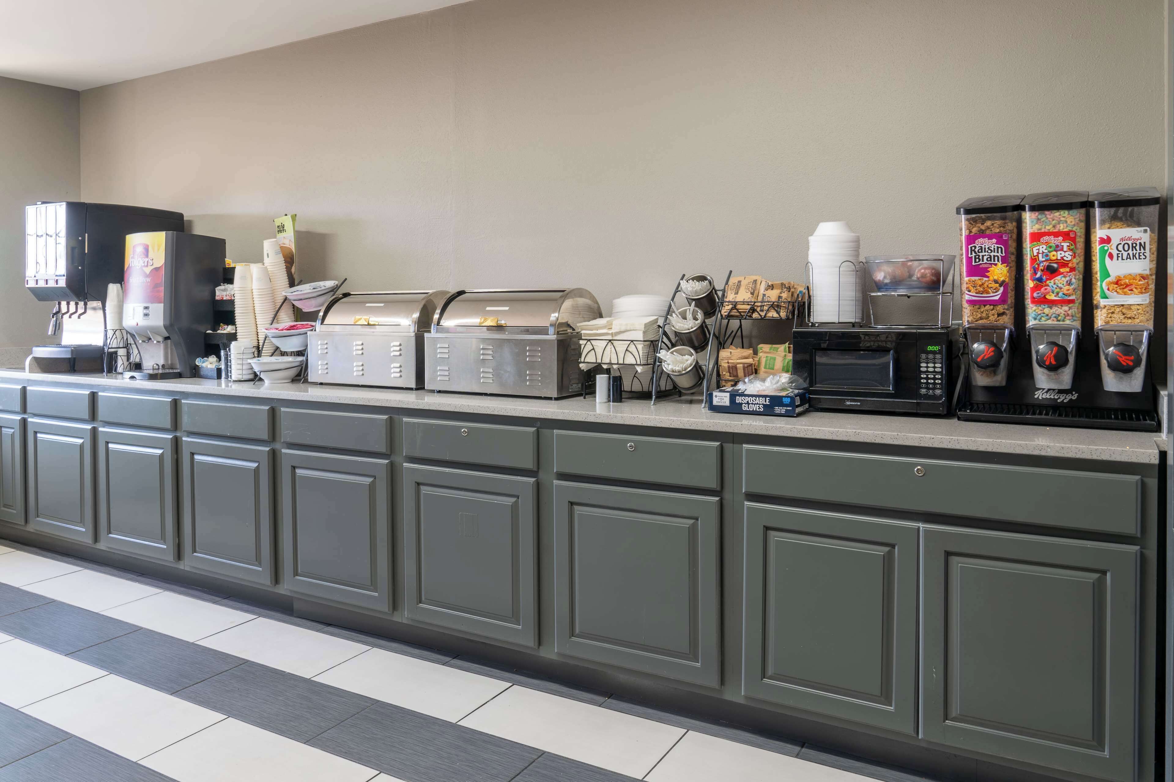 A self-service breakfast station with coffee machines, cereal dispensers, and a microwave.