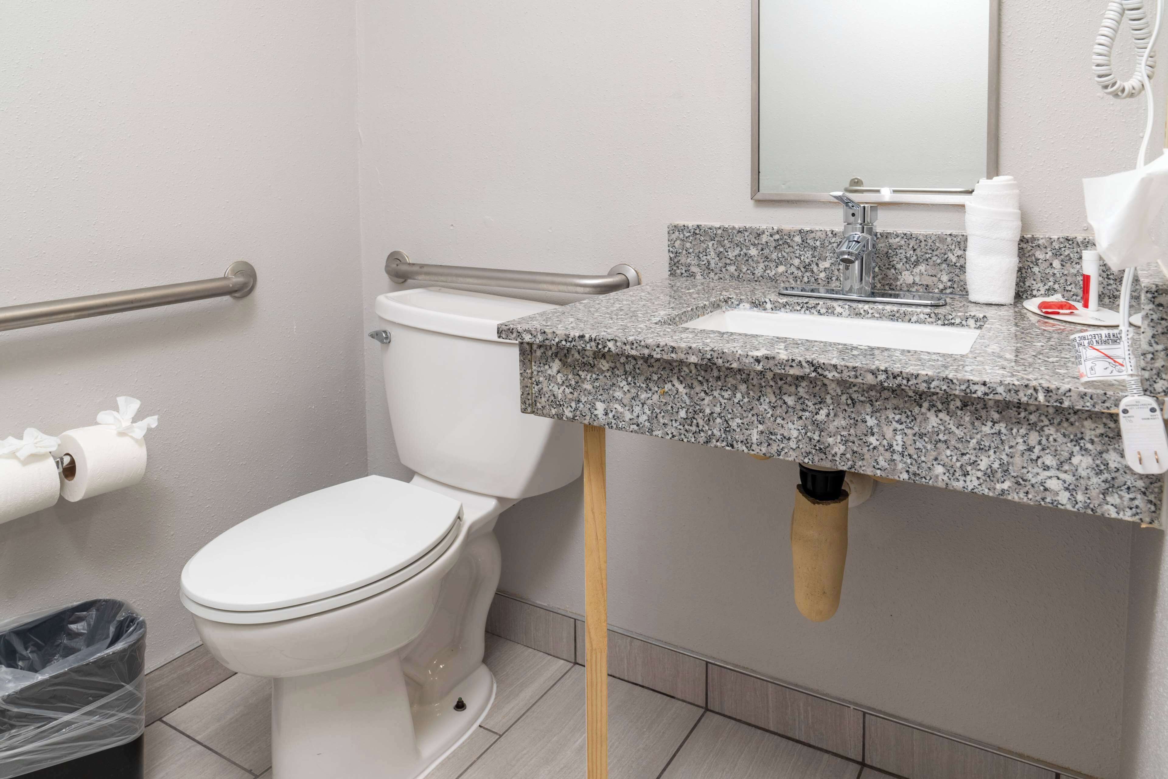 A bathroom with a white toilet, a granite countertop sink, a mirror, and a hand dryer.