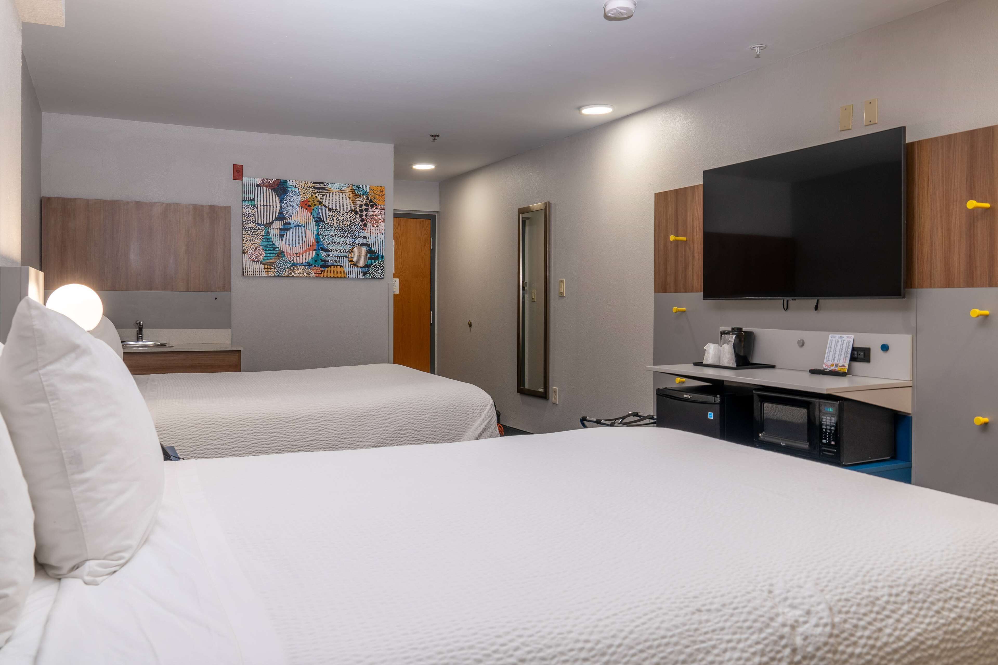 A hotel room with two beds, a flat-screen TV, a microwave, and a small kitchenette.