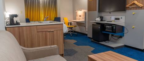 Una habitación de hotel compacta con kitchenette, un sofá, un escritorio y un televisor.