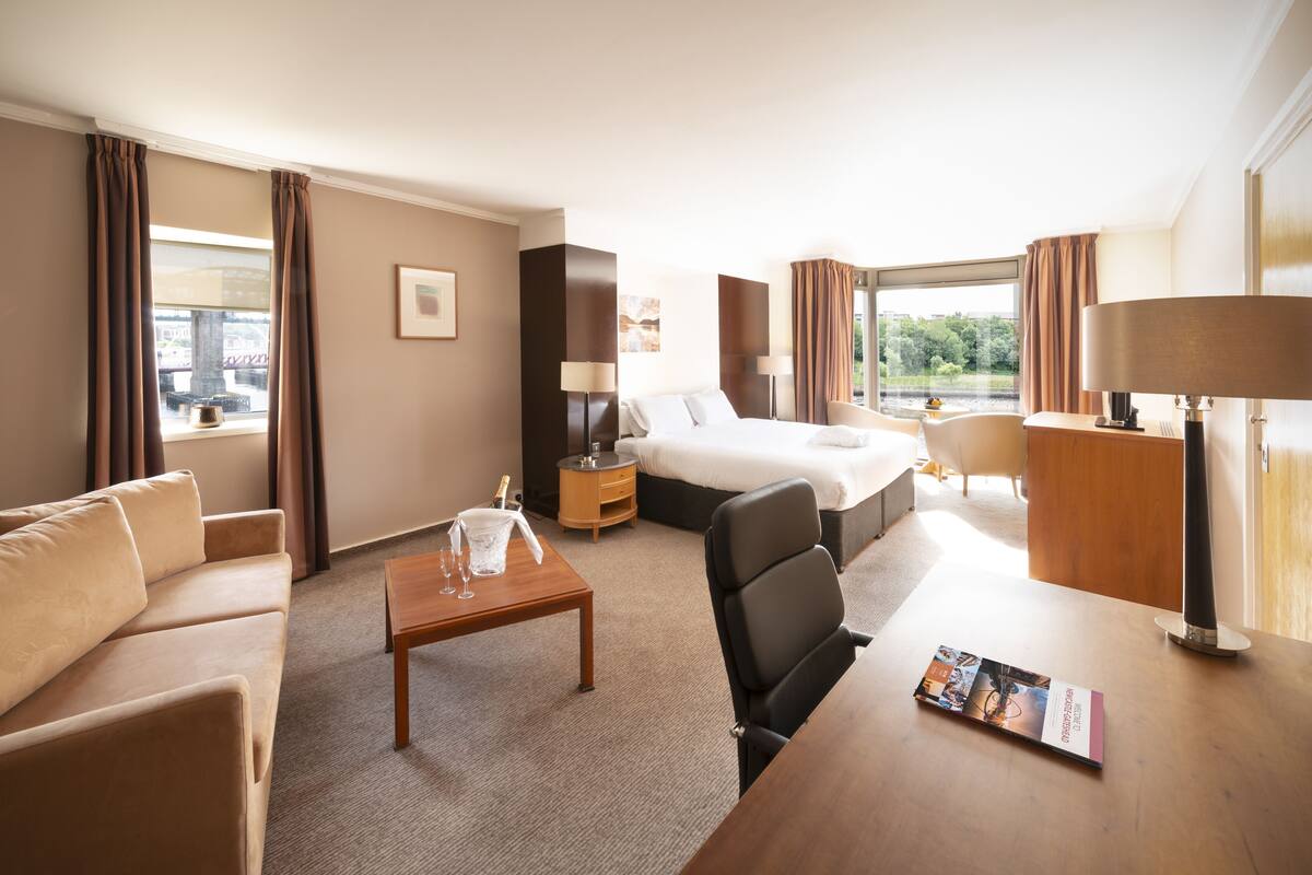 Ein Hotelzimmer mit Bett, Sofa, Schreibtisch und Blick ins Freie.