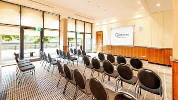Een vergaderzaal met rijen stoelen, een scherm voor presentaties en een bordje met de tekst 'Catherine Newcastle'.