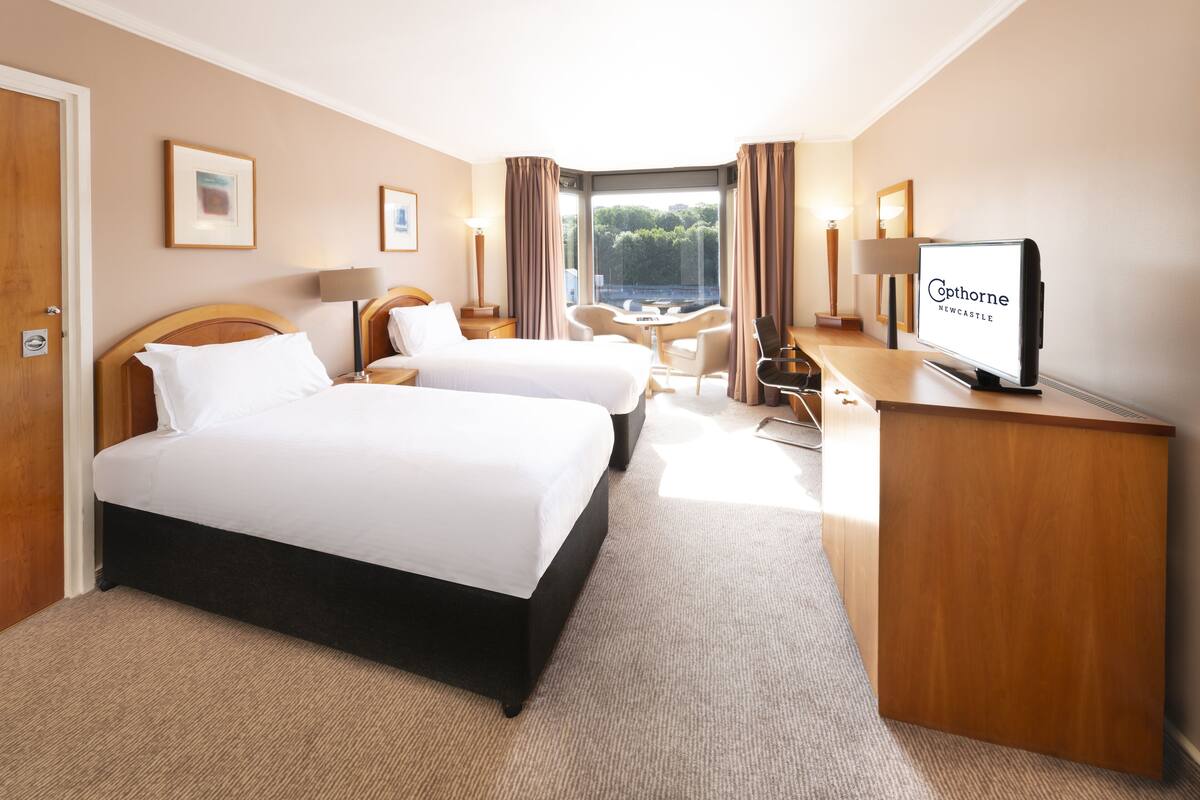 Ein Hotelzimmer mit zwei Betten, einem Schreibtisch, einem Stuhl und einem Fernseher.