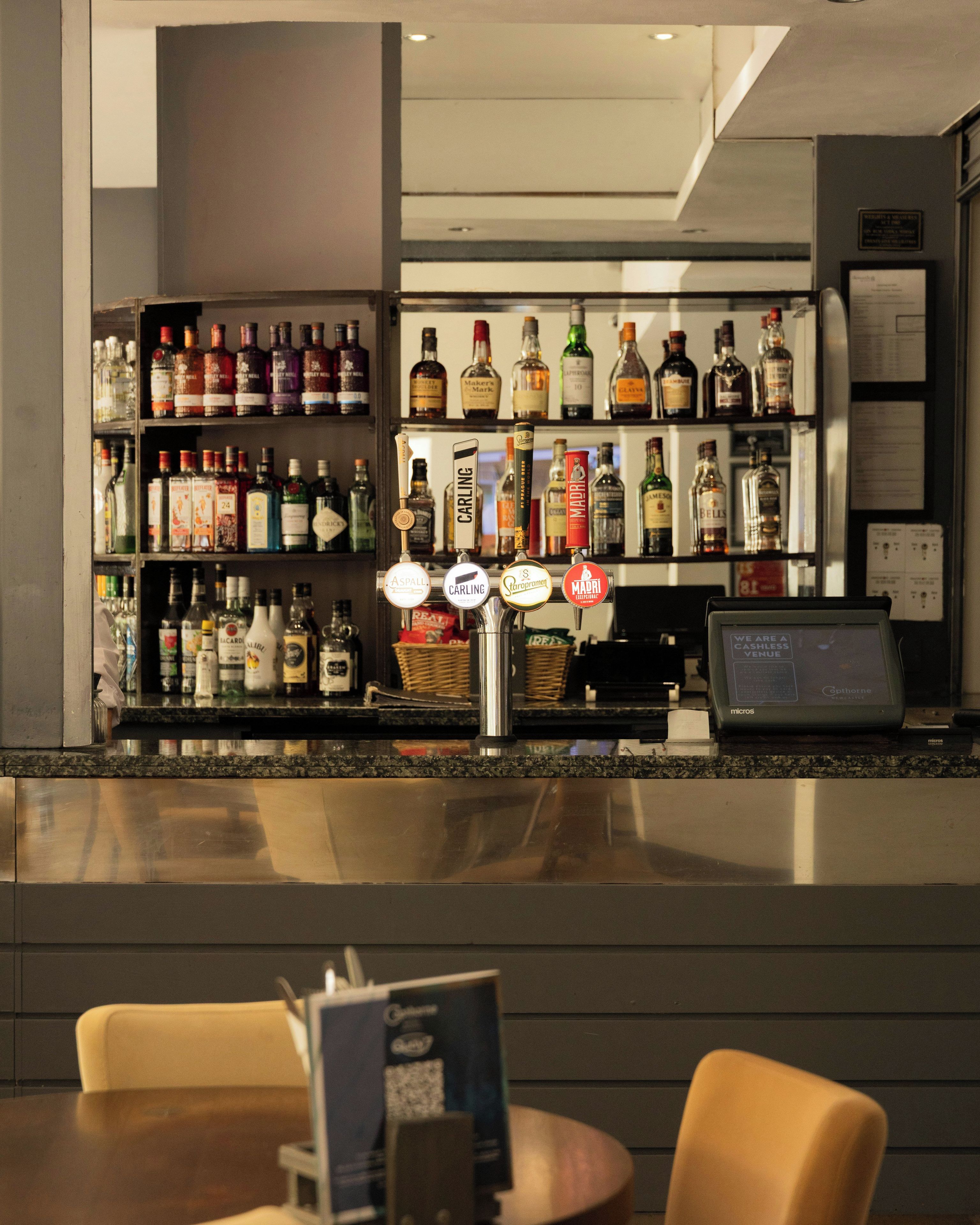 A bar area with shelves of liquor bottles, a cash register, and a seating area with tables and chairs.