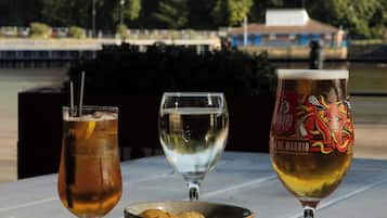 Una mesa con tres vasos de bebidas y un bol de comida, ubicada al aire libre con vistas a árboles y un edificio en el fondo.