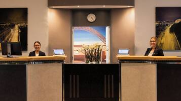 A reception desk with two computer monitors, a clock, and a large window displaying a cityscape.