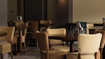 A hotel dining area with multiple tables and chairs, a modern light fixture, and a carpeted floor.