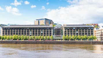 A modern building with a glass facade, located beside a river.