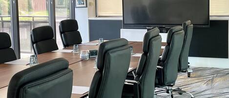 A conference room with a large table, six black office chairs, a flat-screen TV, and a ceiling projector.