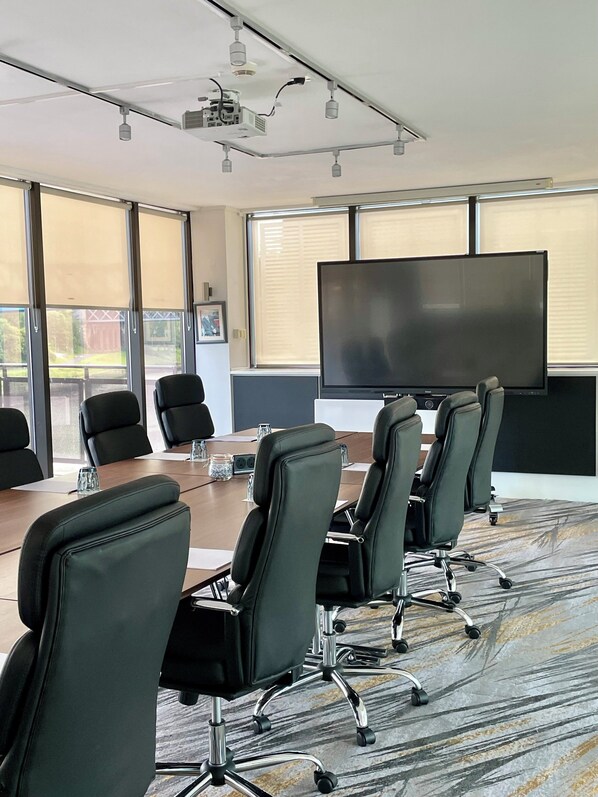A conference room with a large table, six black office chairs, a flat-screen TV, and a ceiling projector.