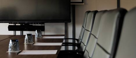 Un salón de conferencias con una pantalla plana grande, una mesa larga y varias sillas de cuero.