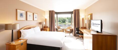 A hotel room with a bed, bedside table, lamp, desk, chair, and a television.