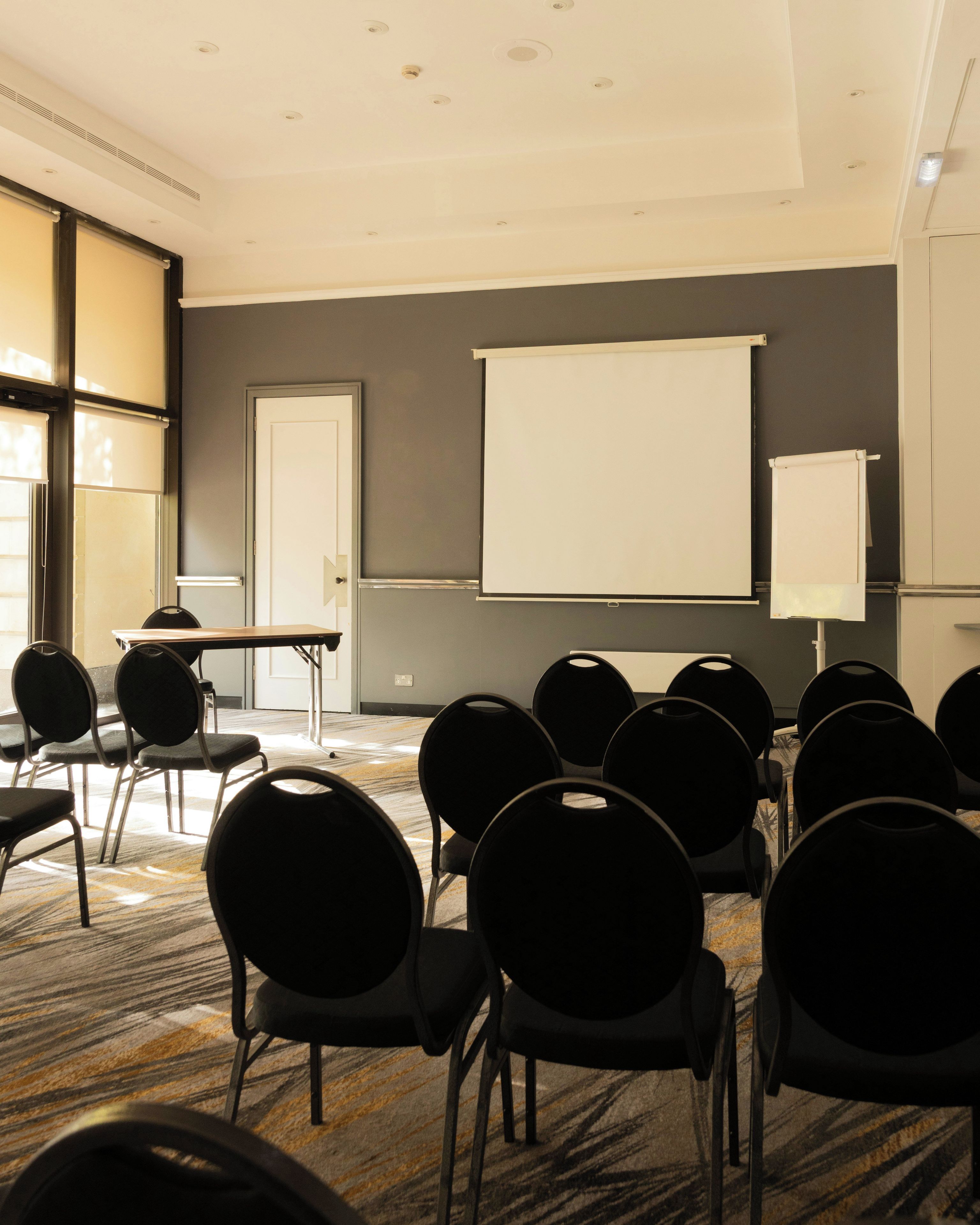 A conference room with a projector screen, a whiteboard, and rows of chairs.