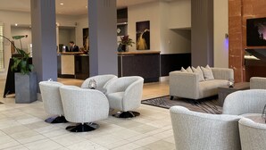 A modern lobby with grey upholstered sofas, a reception desk, and a large painting on the wall. - Copthorne Hotel Newcastle (Newcastle-upon-Tyne)