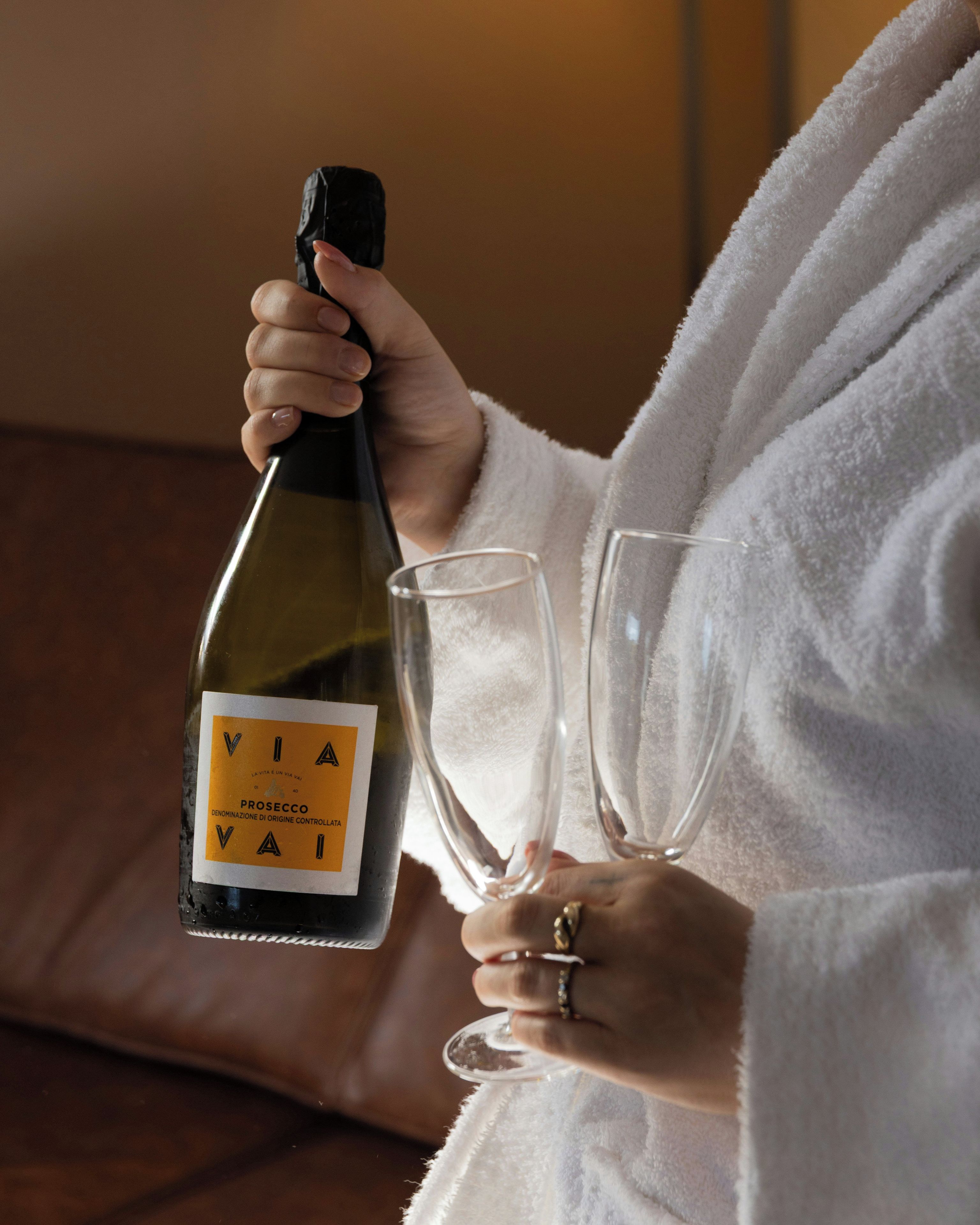 A person holding a bottle of Prosecco wine and two glasses.