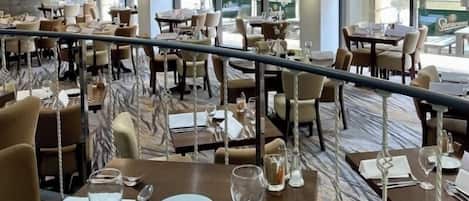 A spacious restaurant with multiple dining tables, chairs, and a view of the outside through large windows.