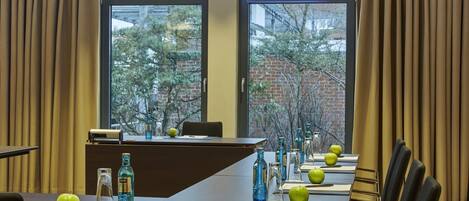 Une salle de conférence dotée d’une longue table, de chaises et offrant une vue sur les arbres et les bâtiments grâce à de grandes fenêtres.