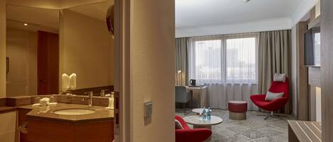 Una habitación de hotel con baño, un área de comedor con mesa y sillas, y un televisor montado en la pared.