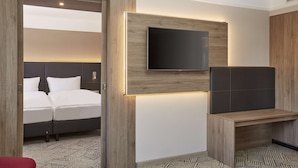 A hotel room with a bed, a TV mounted on the wall, and a wooden desk. - H4 Hotel Hannover Messe (Laatzen)