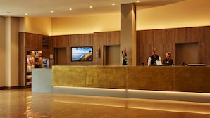 A hotel reception area with a modern design, featuring a reception desk, a television screen, and a decorative vase with flowers. - H4 Hotel Hannover Messe (Laatzen)
