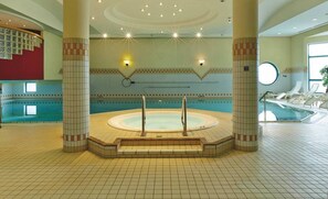 A large indoor swimming pool with a hot tub in the center, surrounded by tiled walls and columns. - H4 Hotel Hannover Messe (Laatzen)