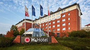 A hotel with a prominent sign, multiple flags, and a modern building facade. - H4 Hotel Hannover Messe (Laatzen)