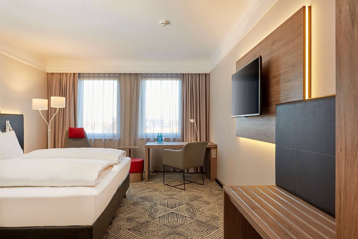A hotel room with a bed, desk, chair, TV, and curtains.