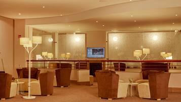 A hotel lobby with a curved ceiling, a large mirror, a television, and several seating areas with brown and beige furniture.
