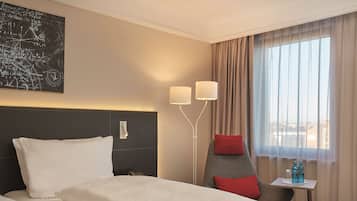 A hotel room with a large bed, a desk with two lamps, a chair, and a window with curtains.