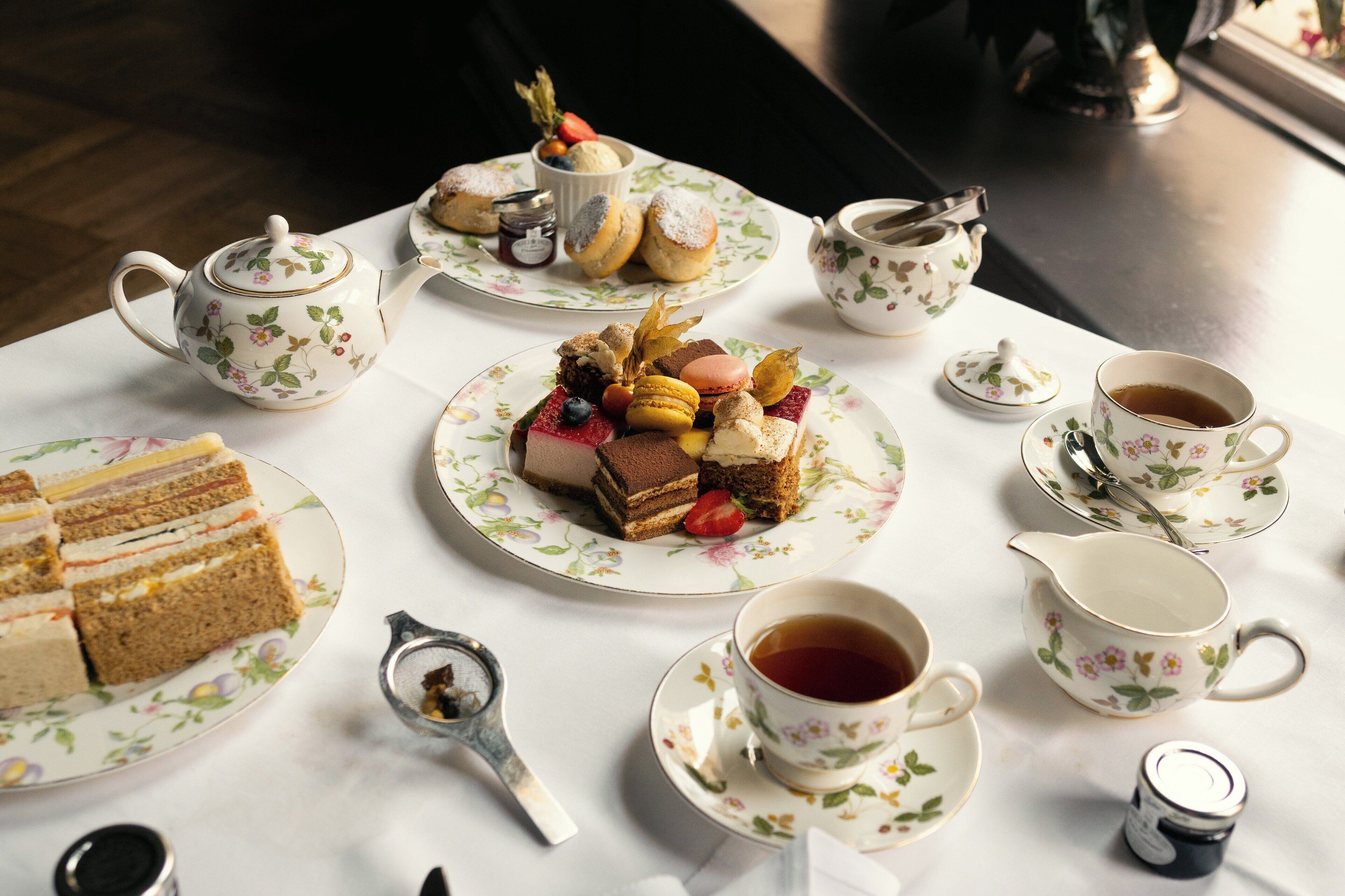 Una mesa dispuesta con tazas de té, teteras, un azucarero y diversos pasteles y sándwiches.