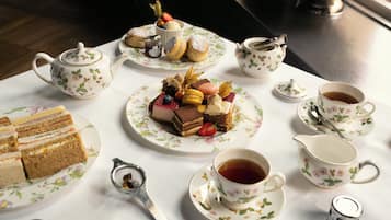 Una mesa dispuesta con tazas de té, teteras, un azucarero y diversos pasteles y sándwiches.