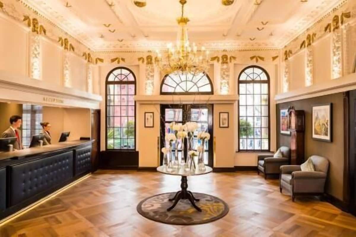 Un vestíbulo de hotel con mostrador de recepción, una araña de cristal y una mesa redonda con flores.