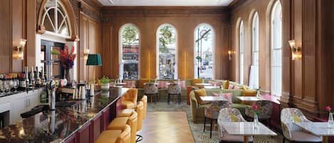 A bar area with a long counter, multiple bar stools, and a variety of bottles and glasses.