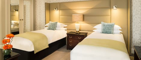 A hotel room with two beds, a nightstand with a lamp, a mirror, and a vase with flowers.