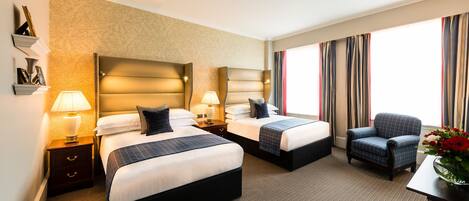 A hotel room with two beds, a chair, a desk, and a large window with curtains.