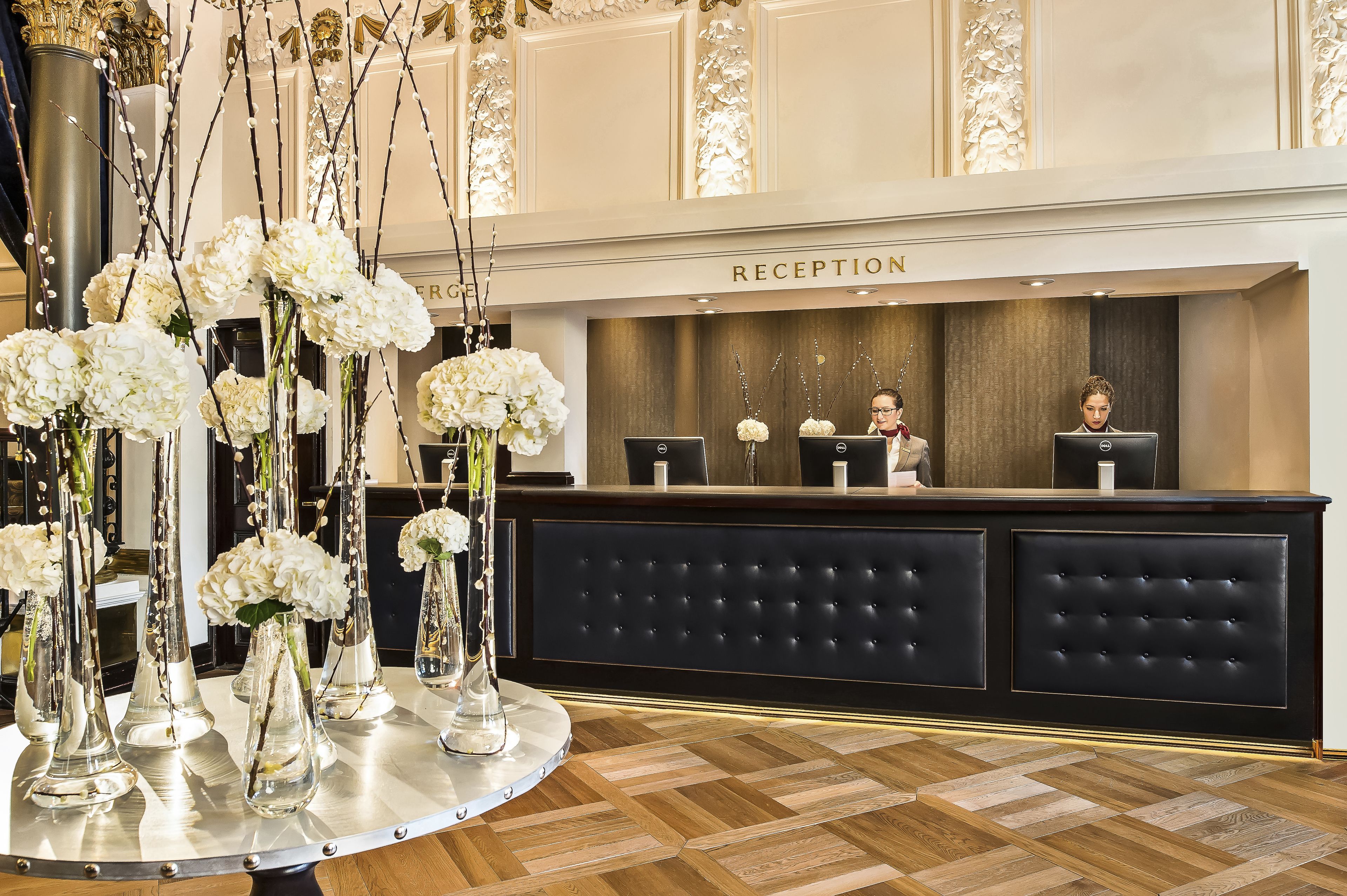 A reception area with a black tufted desk, white flowers in glass vases, and a sign that reads "RECEPTION".