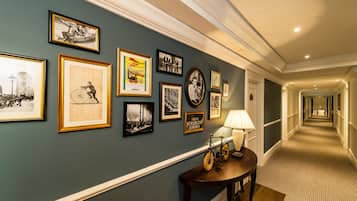 A hallway with framed pictures on the wall, a lamp on a table, and a carpeted floor.