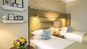 Camera d'albergo con due letti, un comodino con una lampada, un vaso con fiori e quadri incorniciati su mensole.