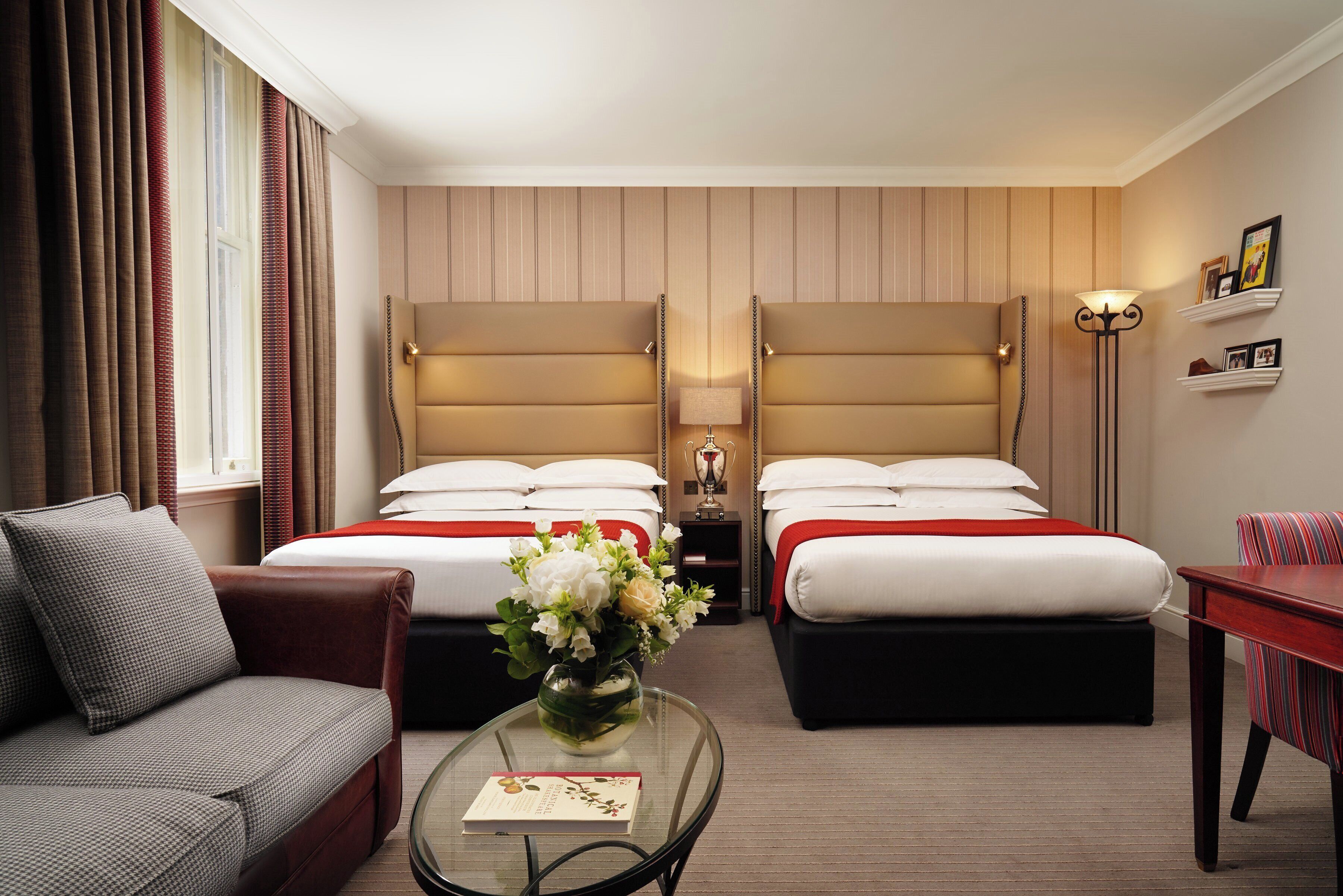 A hotel room with two beds, a sofa, a coffee table with a book, and a vase of flowers.