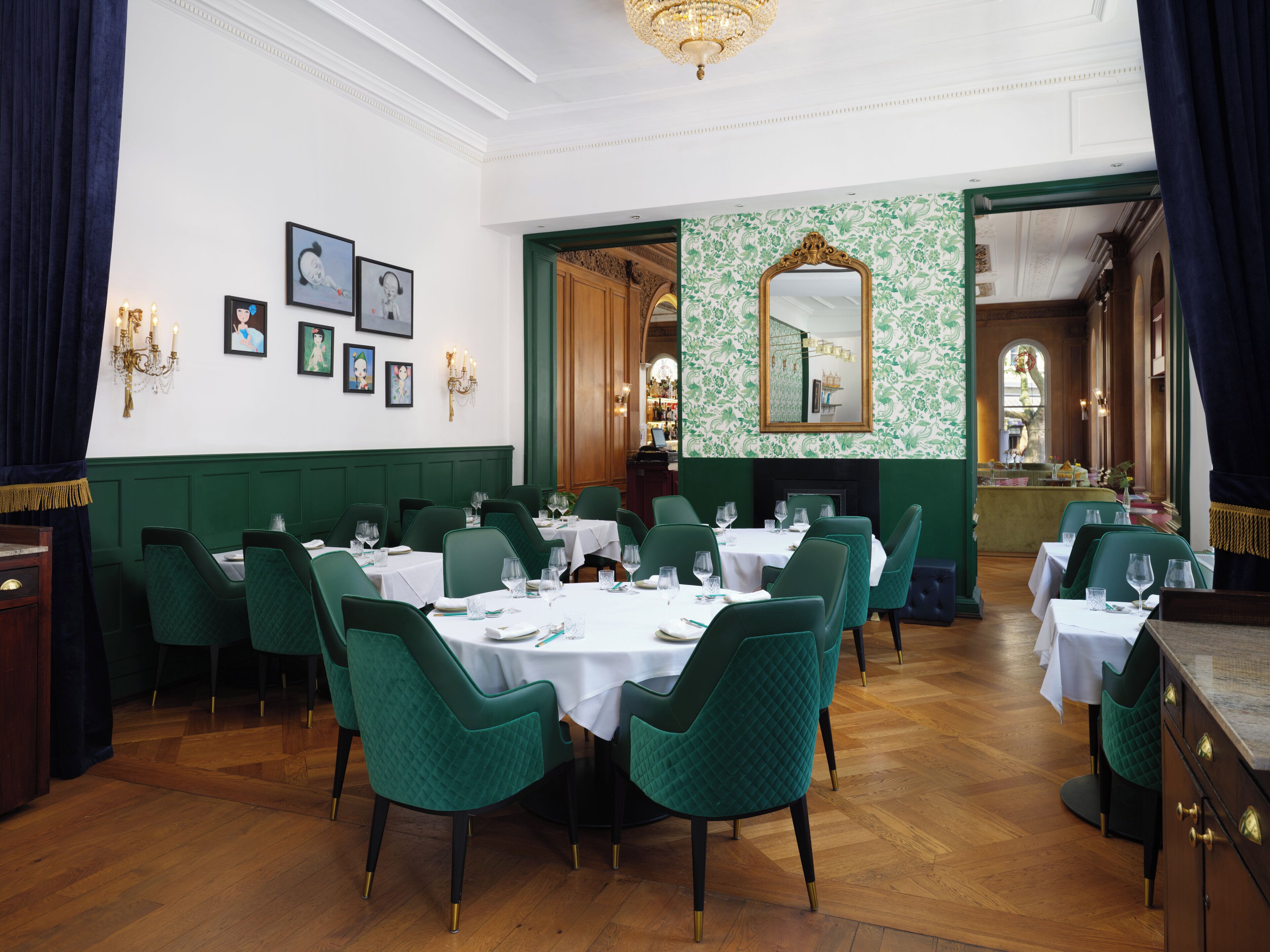 A formal dining room with green upholstered chairs, white tablecloths, and a chandelier.