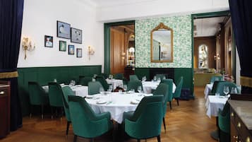 Un comedor formal con sillas tapizadas en verde, manteles blancos y una araña.