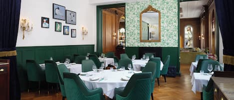 Un comedor formal con sillas tapizadas en verde, manteles blancos y una araña.
