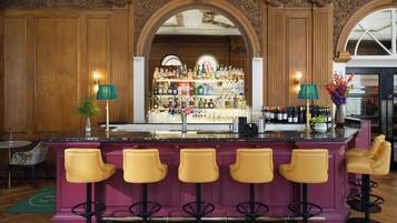 A bar area with a marble countertop, multiple stools, and a well-stocked shelf of bottles.