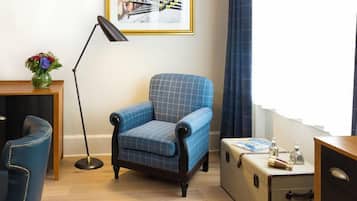 Una habitación con un sillón azul, una lámpara de pie, una maleta y un cuadro en la pared.