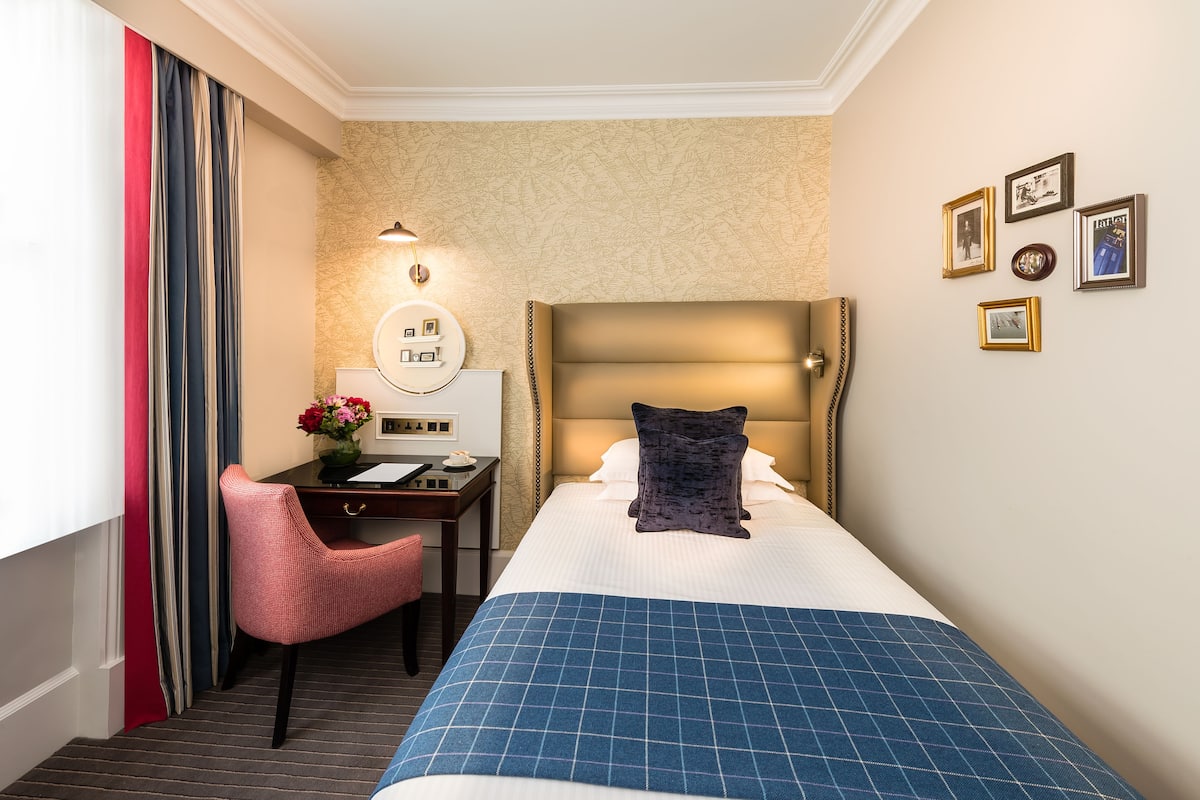 Habitación de hotel con cama, escritorio, silla, lámpara y cuadros en la pared.
