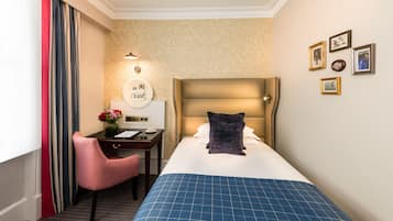 Habitación de hotel con cama, escritorio, silla, lámpara y cuadros en la pared.