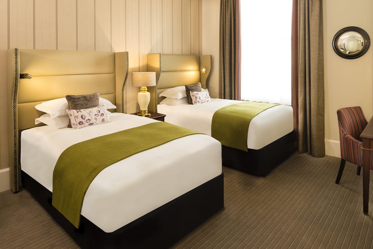 Habitación de hotel con dos camas, un espejo, una silla y una lámpara.